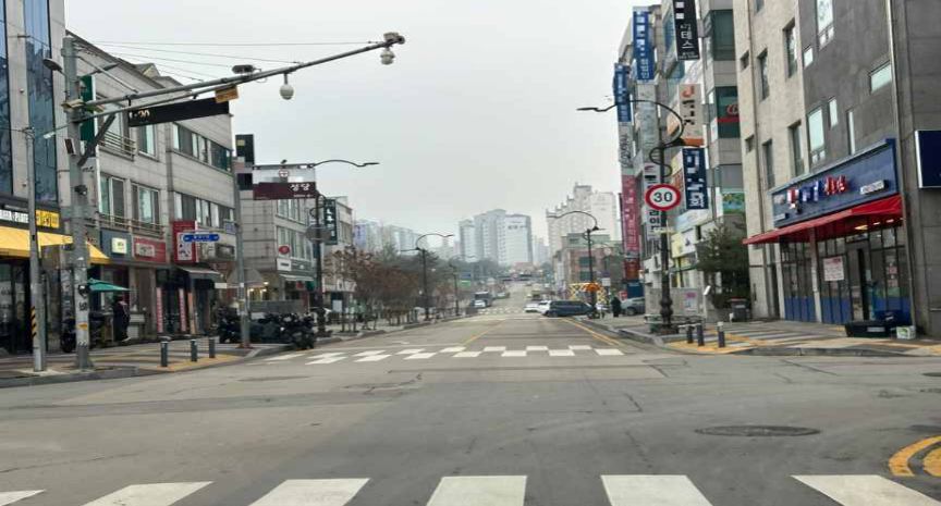 ทางแยกสี่แยกในเขตเมือง · ถนนที่มี 1 ช่องจราจรในแต่ละทิศทาง · ข้างหน้าประมาณ 10 เมตร มีทางเข้าลานจอดรถใต้ดินของอาคารร้านค้าทั้งทางซ้ายและทางขวา