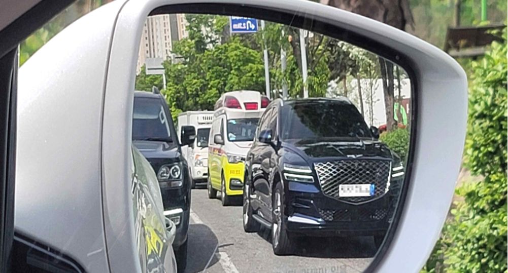 Дорога с двумя полосами в каждом направлении · В правом боковом зеркале видна машина экстренной службы на вызове в полосе 2 · Плотное движение, затор