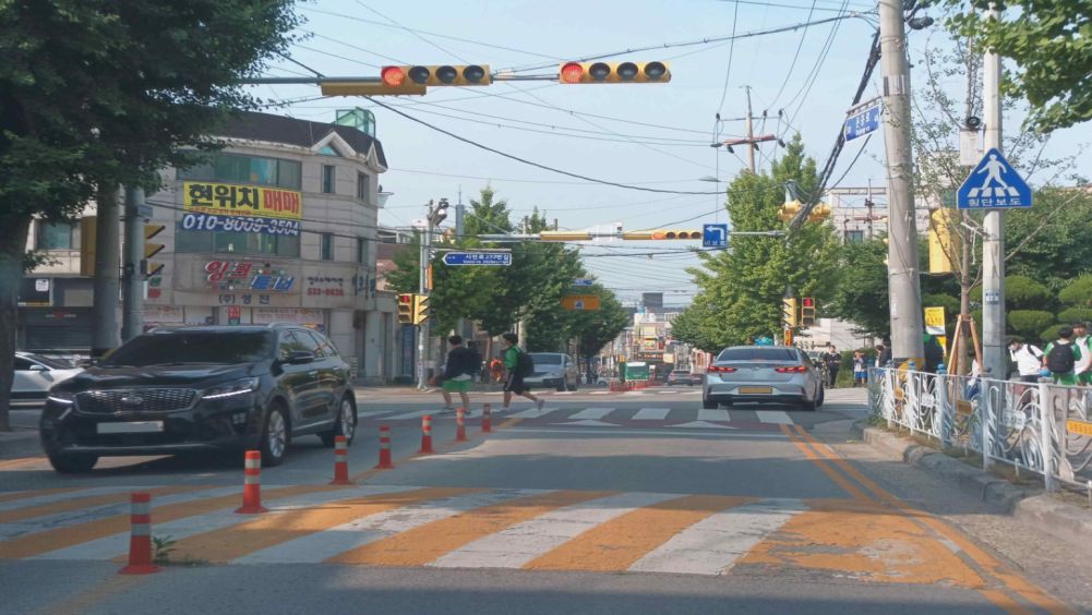 Crosswalk in a children's protection zone · Vehicle light ahead is red; children are crossing on the green pedestrian light · Safety sign reading "Unprotected left turn"