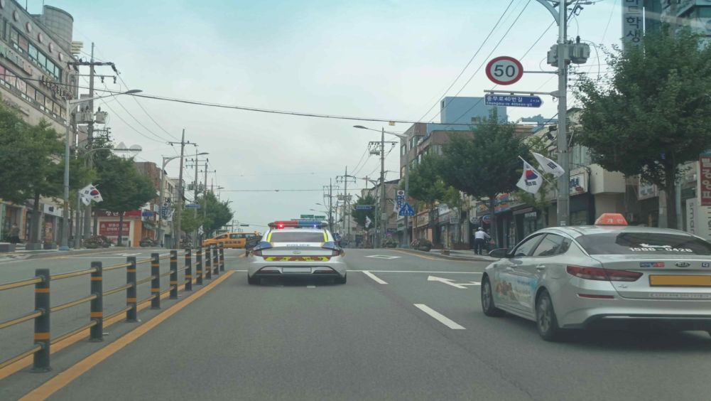 Several police patrol cars on an emergency call with sirens and flashing lights on · A taxi ahead on the right is going straight · Four-way intersection